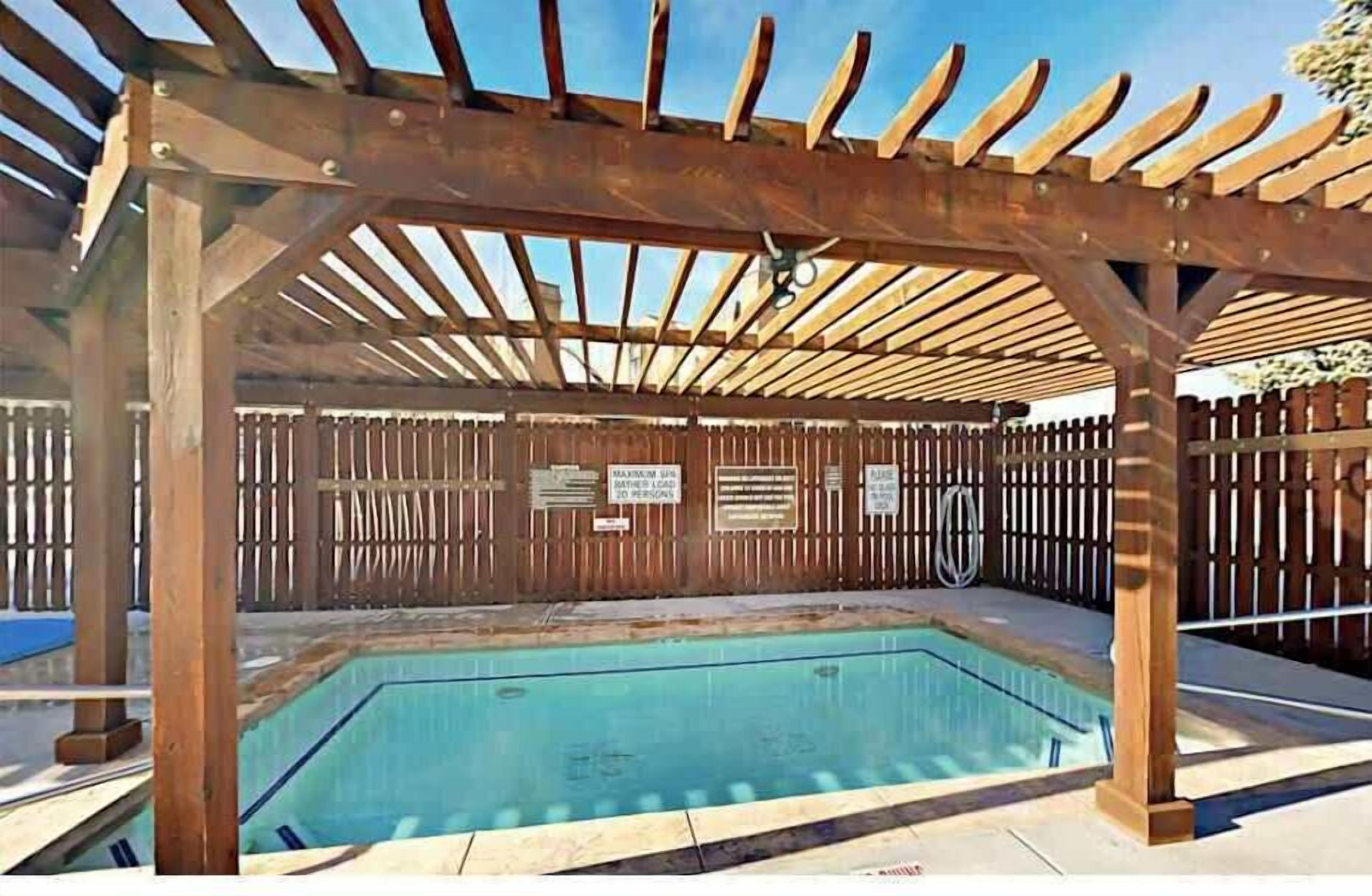 A wooden pergola over a swimming pool with a wooden fence and signs on the wall.