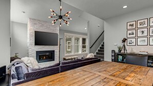 Una sala de estar moderna con chimenea, una gran mesa de comedor de madera, un sofá y un televisor montado.