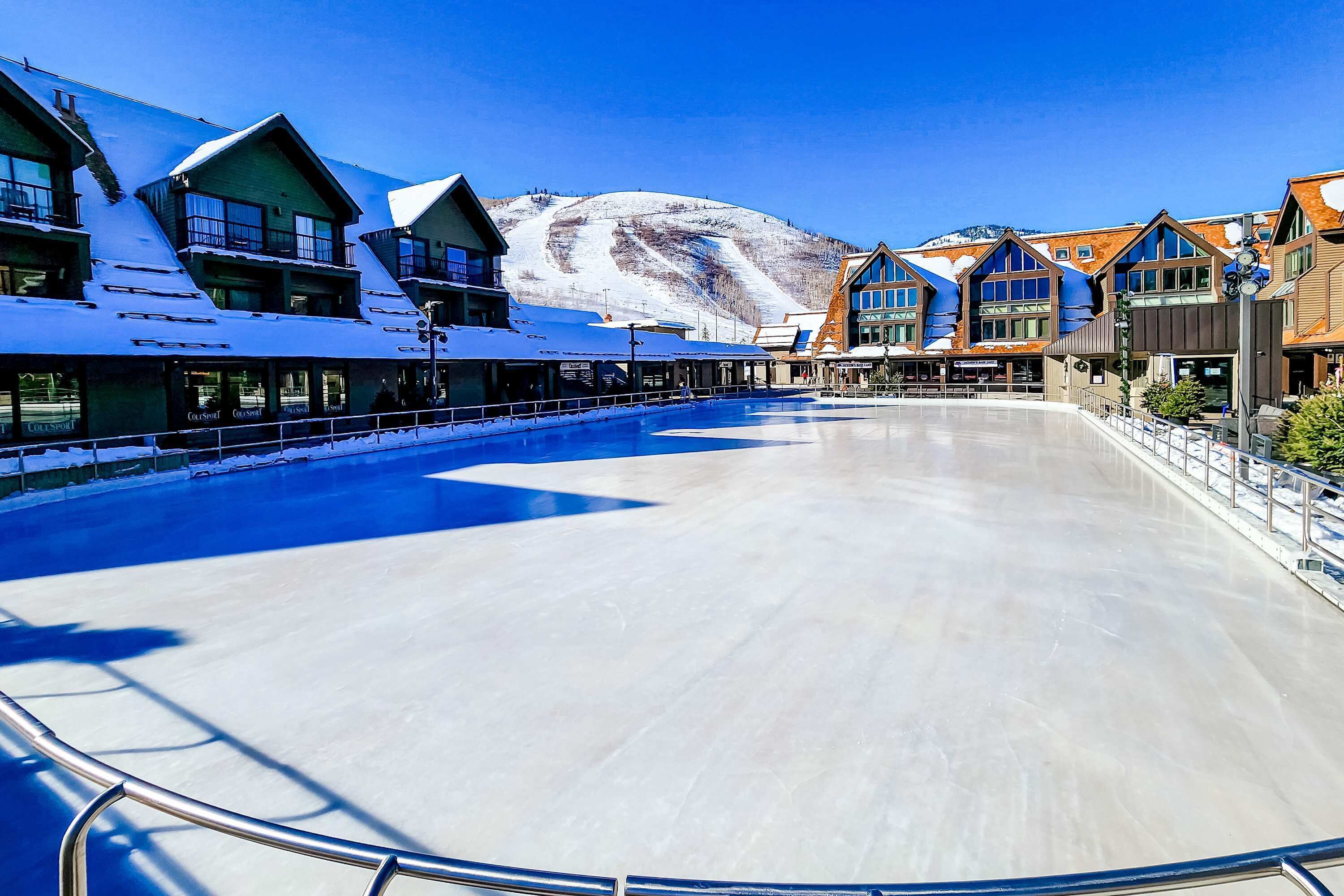 Une patinoire en plein air recouverte de neige, avec des bâtiments en arrière-plan.
