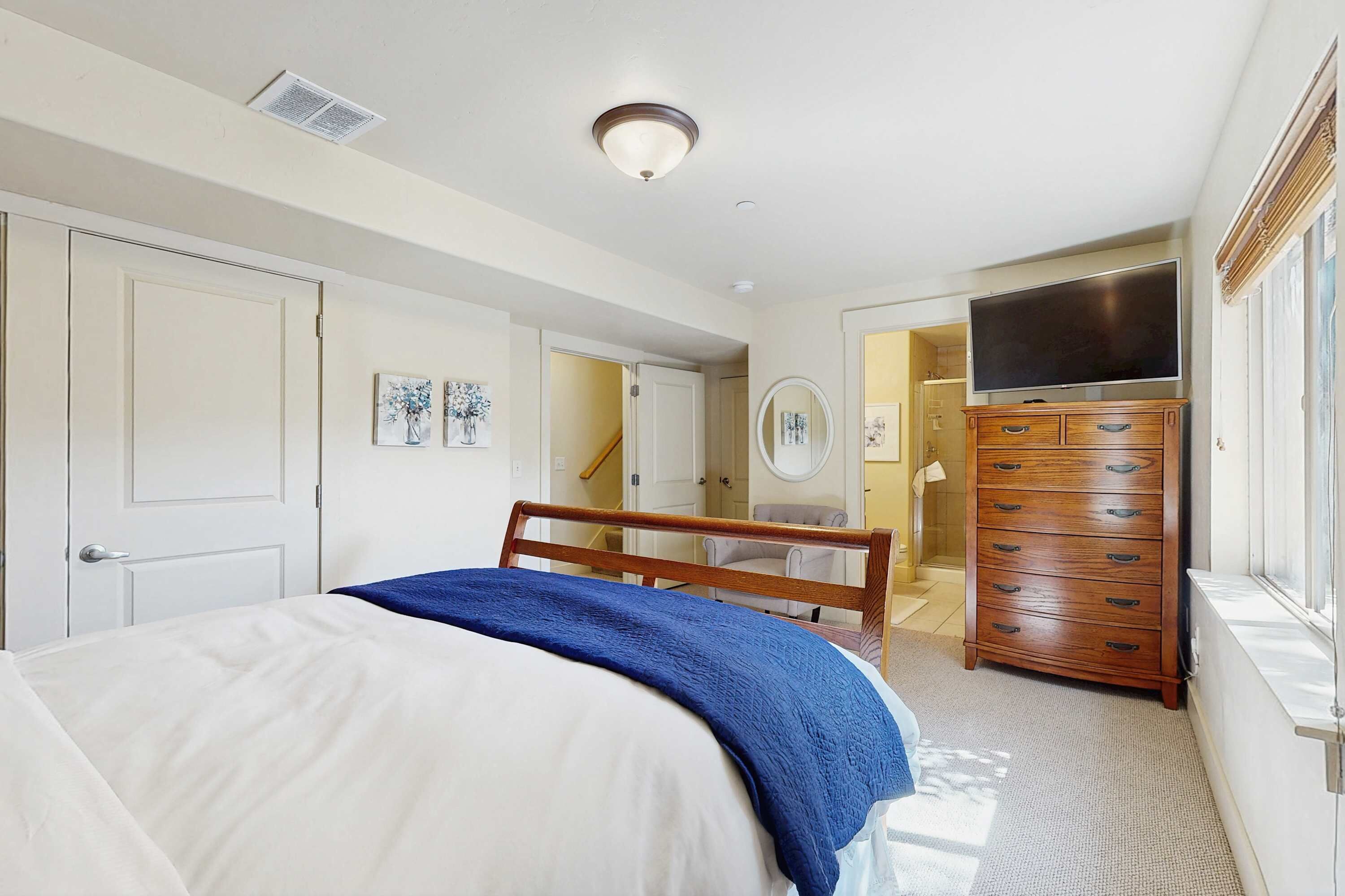 Un dormitorio con cama, cómoda, televisor y puerta al baño.