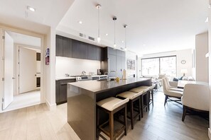 A modern kitchen with a central island, bar stools, and a dining area with a table and chairs. - Pool Deck, Hot Tubs & Gym - Stunning Condo in New Ski-In, Ski-Out Community (Park City)