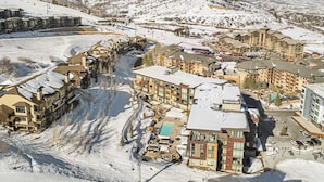 A snow-covered resort with multiple buildings, a ski lift, and a pool area. - Pool Deck, Hot Tubs & Gym - Stunning Condo in New Ski-In, Ski-Out Community (Park City)