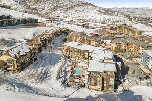 A snow-covered resort with multiple buildings, a ski lift, and a pool area. - Pool Deck, Hot Tubs & Gym - Stunning Condo in New Ski-In, Ski-Out Community (Park City)