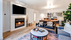 A modern living room with a fireplace, a flat-screen TV, a dining area, and a kitchen in the background. - Beautifully Updated Luxury Condo -Hot Tub - Walk to Town Lift (Park City)