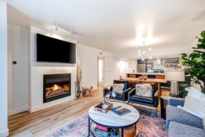 A modern living room with a fireplace, a flat-screen TV, a dining area, and a kitchen in the background. - Beautifully Updated Luxury Condo -Hot Tub - Walk to Town Lift (Park City)