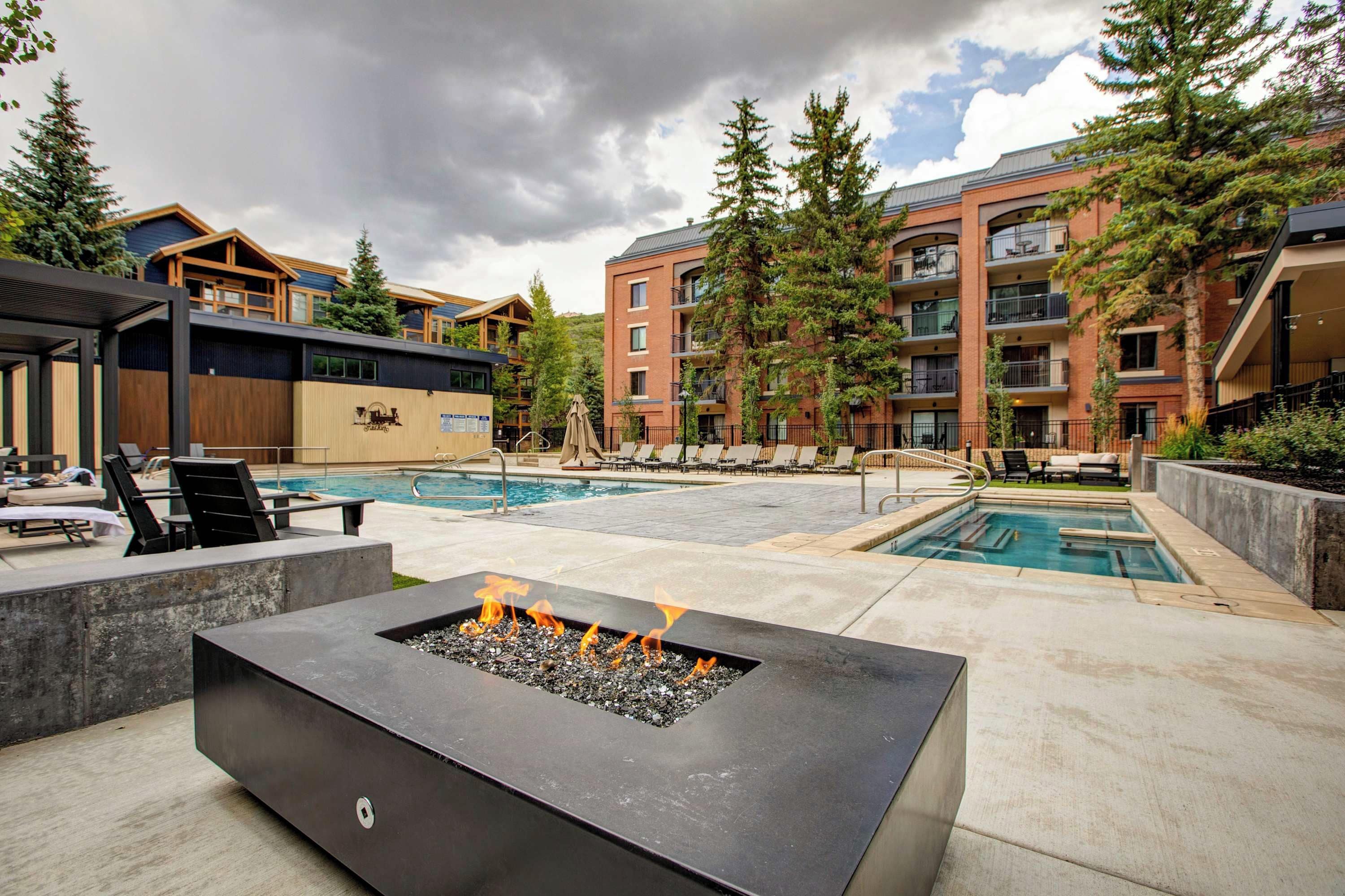 A pool area with lounge chairs, a fire pit, and a building with multiple balconies.