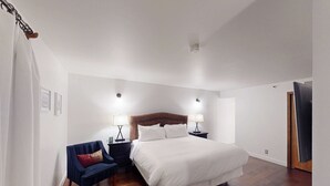 Een slaapkamer met een groot bed, twee nachtkastjes met lampen, een stoel en een houten vloer.