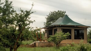 A small, single-story structure with a green roof, surrounded by lush greenery and trees. - Mimark Serengeti Luxury Camp (Serengeti)