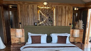 A large bed with a wooden headboard, two bedside tables with lamps, and a wooden floor. - Mimark Serengeti Luxury Camp (Serengeti)