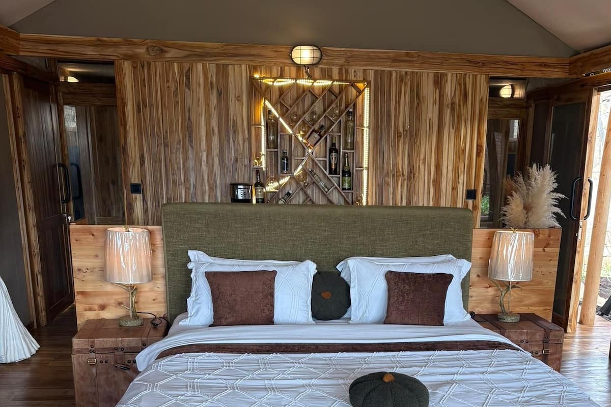 Una cama grande con cabecera de madera, dos mesitas de noche con lámparas y suelo de madera.