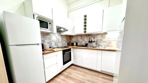 Eine kompakte Küche mit weißen Schränken, einer Mikrowelle, einem Toaster und einer Holzausziehtafel.