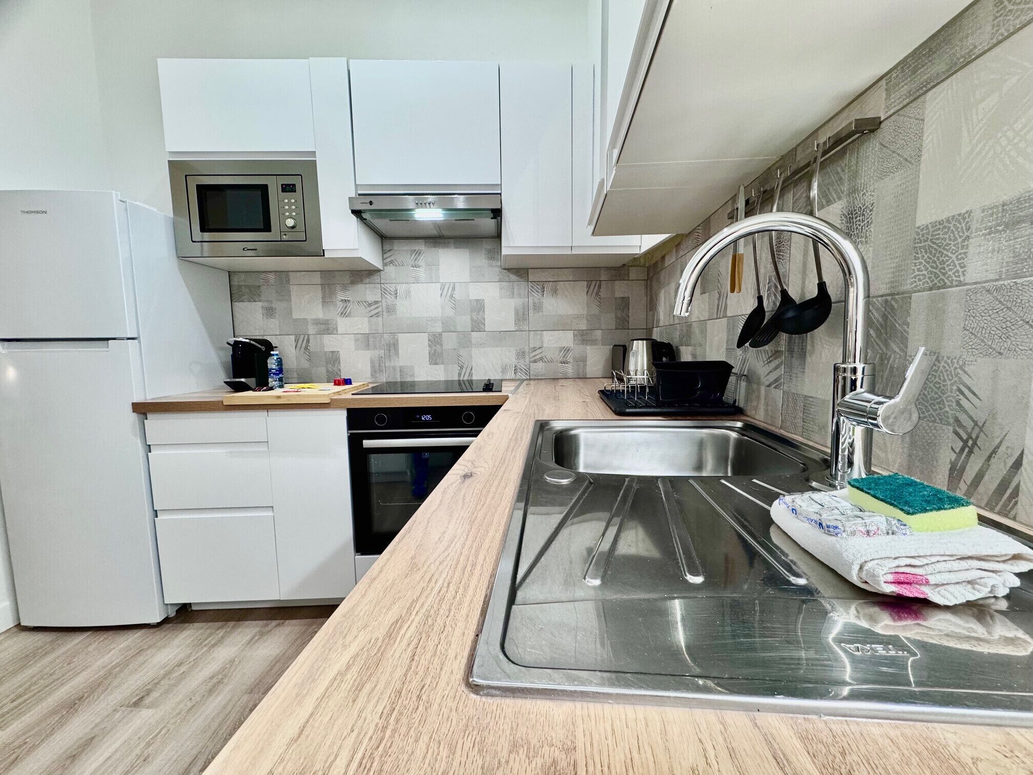 Una cucina moderna con mobili bianchi, un lavello in acciaio inossidabile, un forno a microonde ed una lavastoviglie.