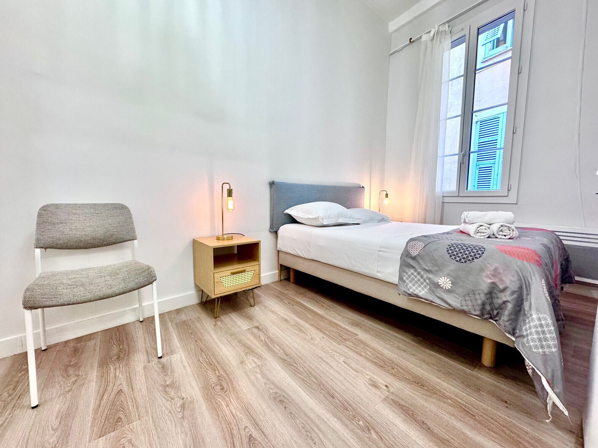 Une chambre à coucher avec un lit, une table de chevet, une chaise et une fenêtre avec des rideaux.