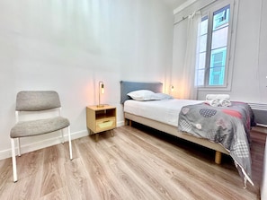 Une chambre à coucher avec un lit, une table de chevet, une chaise et une fenêtre avec des rideaux.