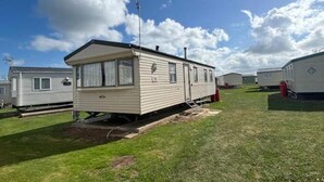 A mobile home with a small porch, a chimney, and a satellite dish. - Seaside Tranquility Retreat in Clacton (Clacton-on-Sea)