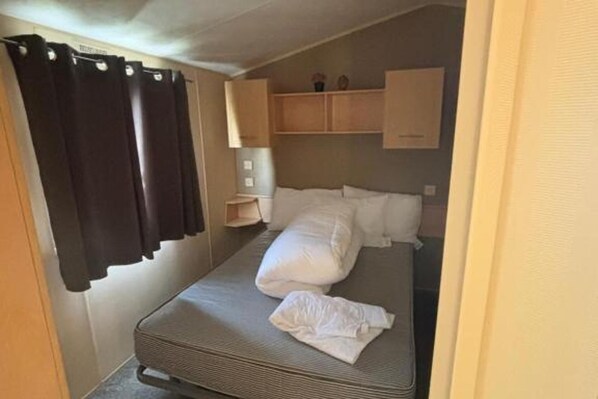 A compact room with a bed, a small bedside table, and a shelf above the bed. - Seaside Tranquility Retreat in Clacton (Clacton-on-Sea)
