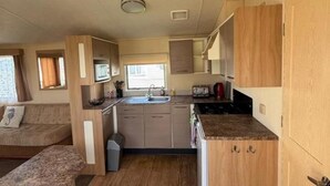 A compact RV kitchen with a sink, stove, and microwave, a small dining area, and a couch. - Seaside Tranquility Retreat in Clacton (Clacton-on-Sea)