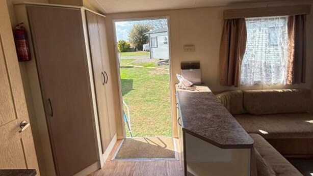 A compact living space with a kitchenette, a sofa, and a door leading to a small outdoor area. - Seaside Tranquility Retreat in Clacton (Clacton-on-Sea)