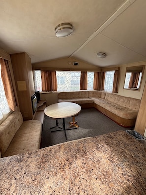 A compact RV interior with a sectional sofa, a round table, and a kitchenette area. - Seaside Tranquility Retreat in Clacton (Clacton-on-Sea)