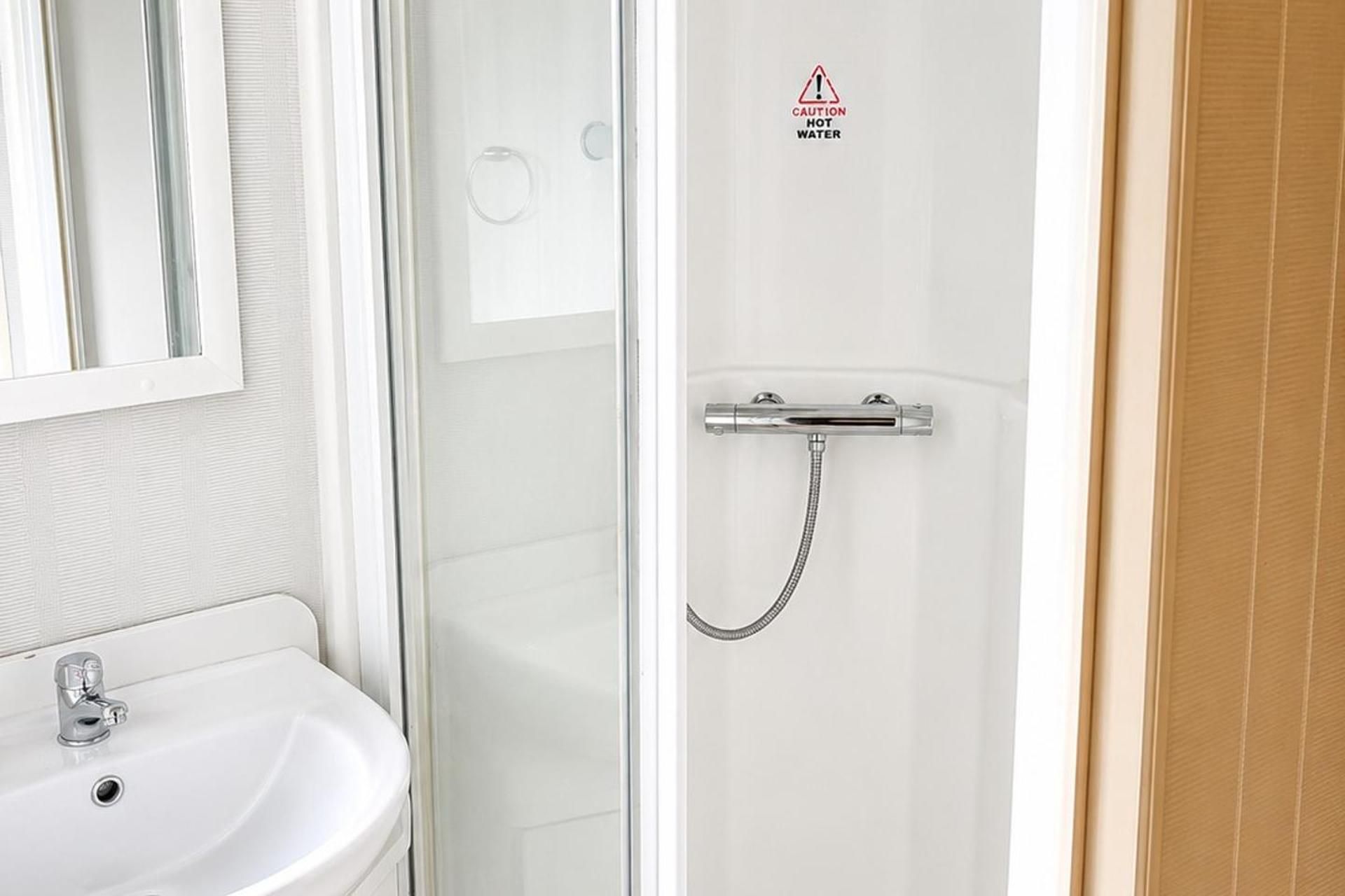 Ein Badezimmer mit Dusche, Waschbecken und einem Warnhinweis wegen heißem Wasser.