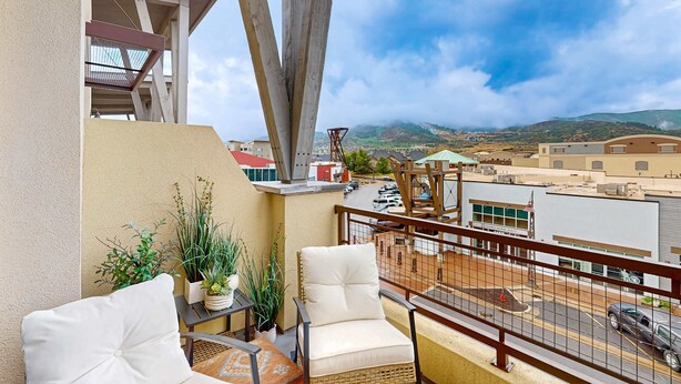A balcony with a view of a cityscape, a chair, a small table with plants, and a railing. - Inviting condo in Newpark Town Center with hot tub and great balcony views (Park City)