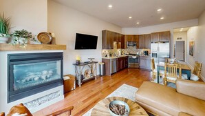 A modern living room with a fireplace, a dining area, and a kitchen with wooden cabinets and stainless steel appliances. - Inviting condo in Newpark Town Center with hot tub and great balcony views (Park City)