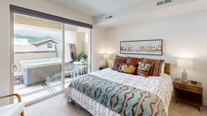 A bedroom with a bed, a nightstand, a lamp, a painting, and a sliding glass door leading to a balcony with a hot tub. - Inviting condo in Newpark Town Center with hot tub and great balcony views (Park City)