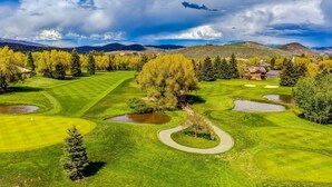 A golf course with a pond, trees, and a mountain range in the background. - Epic view condo with fireplaces & close to everything (Park City)