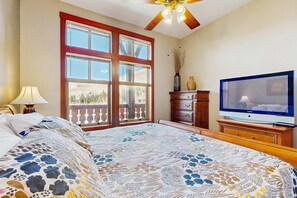 A bedroom with a large bed, a television, a wooden dresser, and a window with a view of trees. - Mountainview Condo with Ski-In/Out Access, Club Solitude Access with Pool & Hot Tub (Solitude)