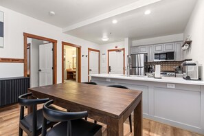A modern kitchen with white cabinets, a stainless steel refrigerator, and a microwave. There is a wooden dining table with four chairs. - Welcoming Condo with a Shared Hot Tub, Pool and Club Solitude Access (Solitude)