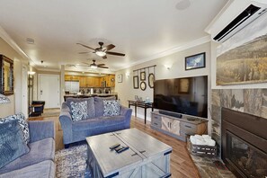 Una sala de estar con sofá, mesa de centro, televisión, chimenea y cocina al fondo.