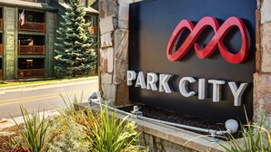 Opastekyltti, jossa lukee ”PARK CITY”, ja jossa on moderni logo. Lisäksi kuvassa on kivirakenteinen rakennus parvekkeineen sekä joulukuusi.