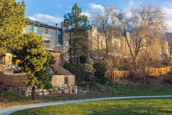 A modern house with a stone foundation, a wooden deck, and a large tree in the foreground. - Updated Condo with Private Hot Tub, Mountain Views, & Gas Grill - Close to Skiing (Cottonwood Heights)