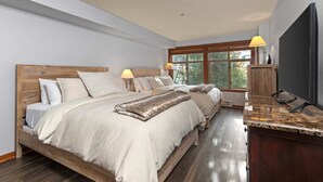 A bedroom with a wooden bed, two bedside lamps, a TV, and a large window. - Lovely Ski-in - ski-out condo with  community hot tub, pool & Club Solitude access (Solitude)