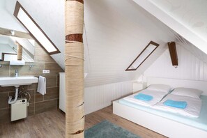 Une chambre moderne dotée d’une lucarne, d’une grande fenêtre, d’un lit et d’une salle de bain avec un lavabo et un miroir.
