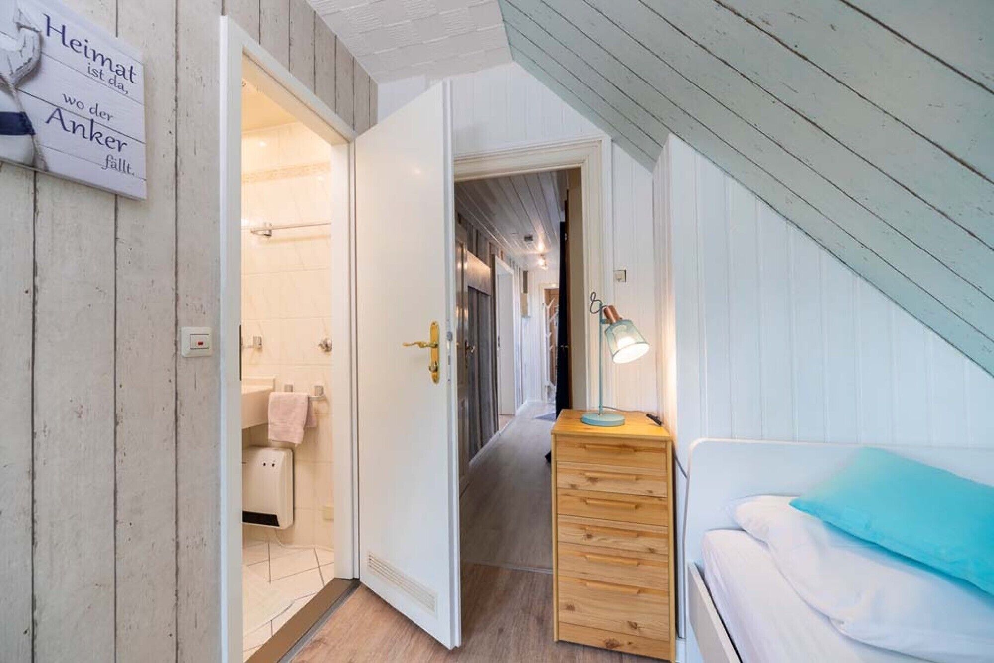 Una camera da letto con un comò in legno, un letto con un cuscino blu e un bagno con un asciugamano appeso al muro.