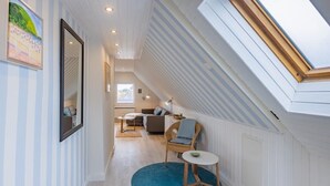 En smal hall med ett takfönster som leder in till ett vardagsrum med en soffa, stolar och ett litet bord.