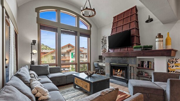 A modern living room with a sectional sofa, a fireplace, and a large window offering a view of a mountain. - Resort Townhome with Deck, Grill, Fireplace, WiFi, Shared Pool & Hot Tub-Sauna (Solitude)