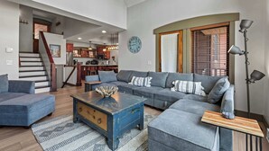 A spacious living area with a large gray sectional sofa, a wooden coffee table, and a staircase leading to an upper level. - Resort Townhome with Deck, Grill, Fireplace, WiFi, Shared Pool & Hot Tub-Sauna (Solitude)