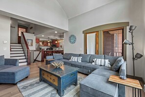 A spacious living area with a large gray sectional sofa, a wooden coffee table, and a staircase leading to an upper level. - Resort Townhome with Deck, Grill, Fireplace, WiFi, Shared Pool & Hot Tub-Sauna (Solitude)