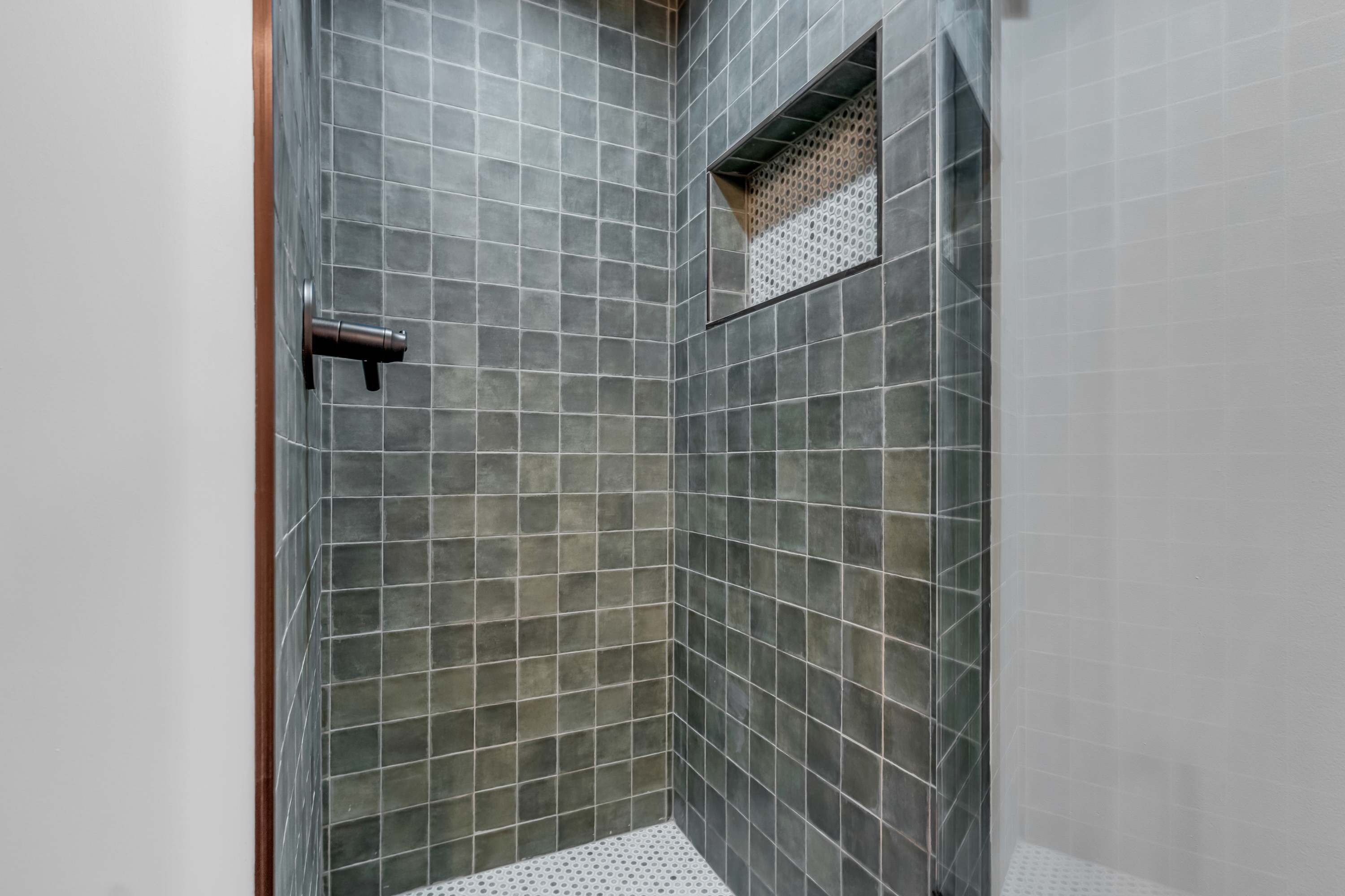 A shower with a tiled wall and a door handle.