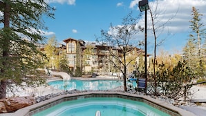 Area piscina con idromassaggio, circondata da alberi e un edificio con diverse finestre.