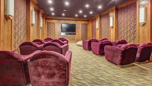 Una sala conferenze con file di sedie viola, un'ampia televisione a schermo piatto, pannelli di legno e luci a incasso.