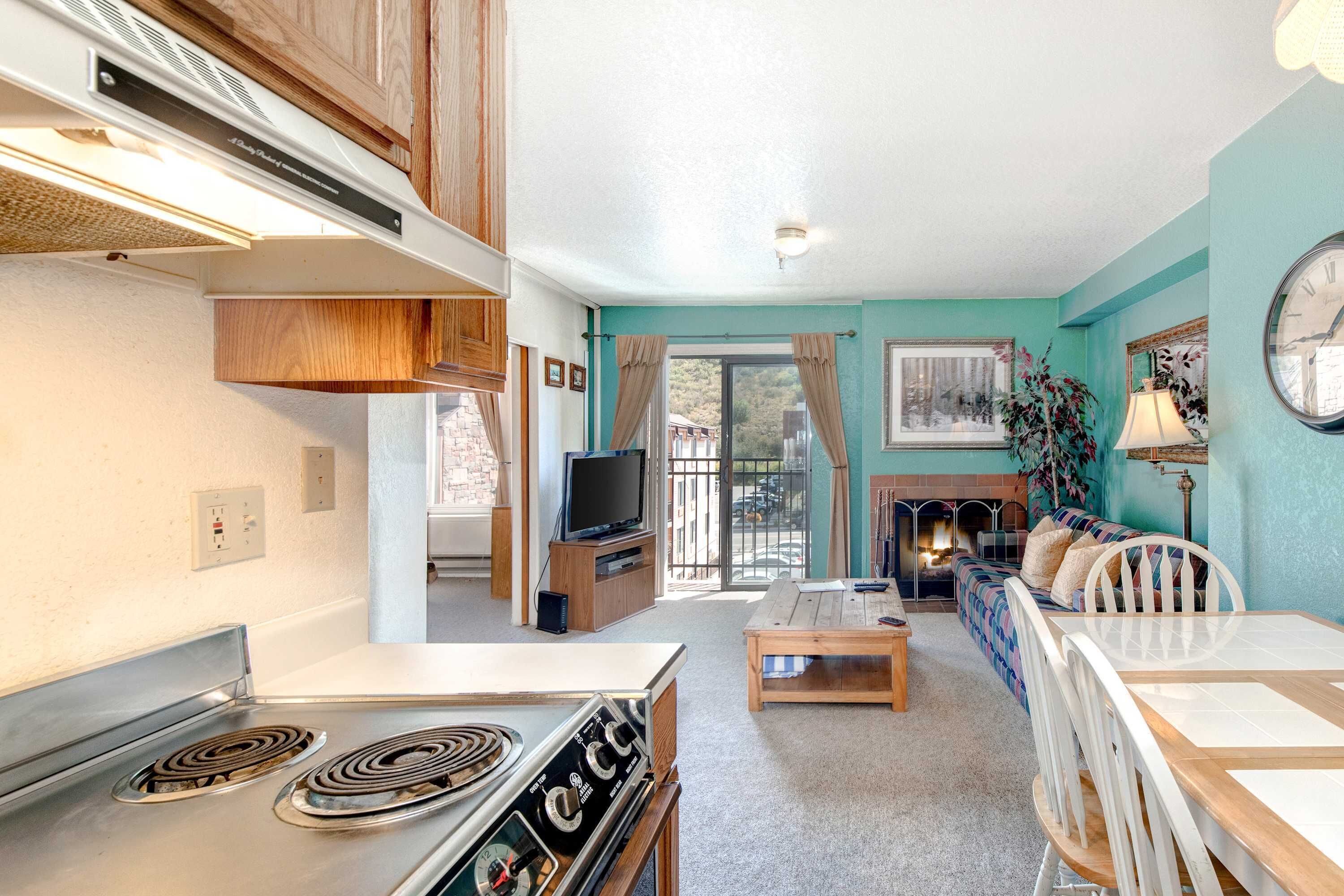 A kitchen with a stove, a dining table with chairs, a sofa, a television, and a fireplace.