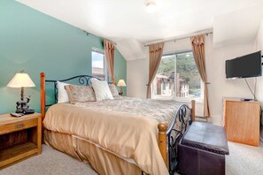 A bedroom with a bed, bedside tables, a TV, and a window with curtains. - Top-floor, mountain view condo with fireplace, pool & hot tub - steps to shuttle (Park City)