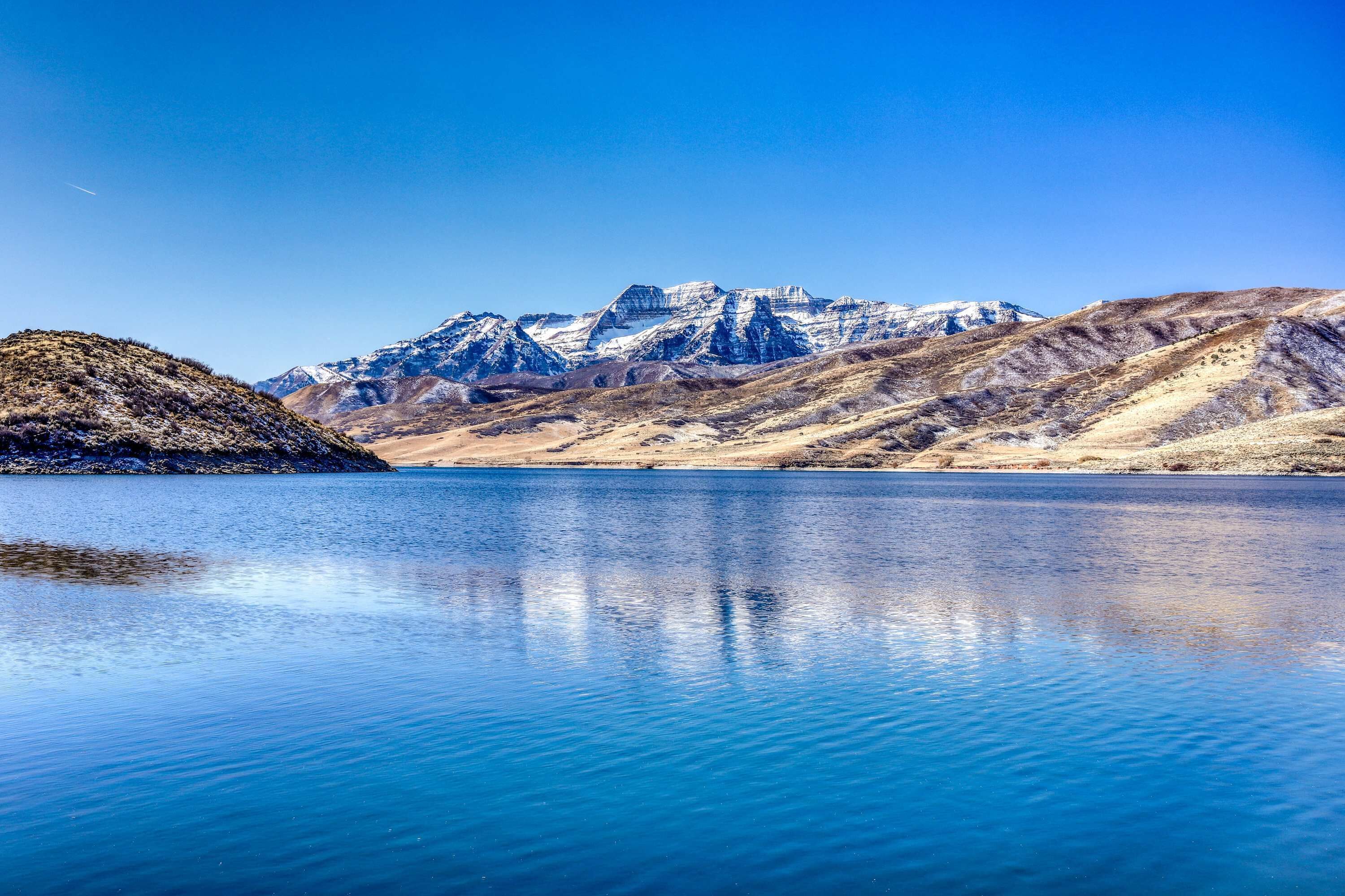 A calm lake with clear blue water reflecting the surrounding mountains.