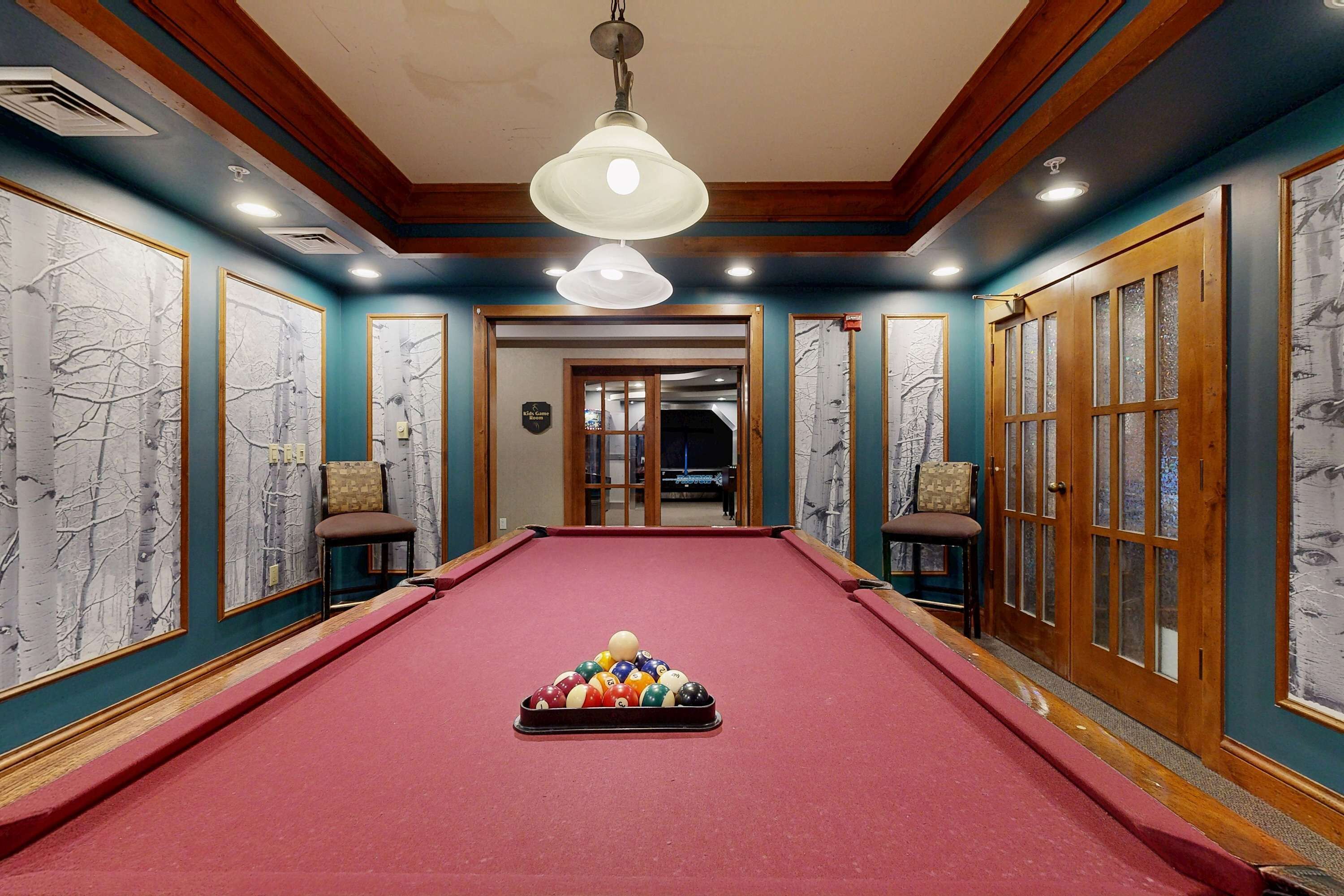 A pool table with balls in the center, flanked by chairs and artwork on the walls.