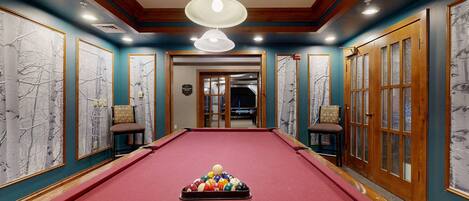 A pool table with balls in the center, flanked by chairs and artwork on the walls.