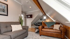 A loft-style living room with a gray sofa, a brown leather armchair, a patterned rug, and a wooden ceiling beam. - Quintessential Historic Old Town-Full Kitchen-Mountain Views (Park City)