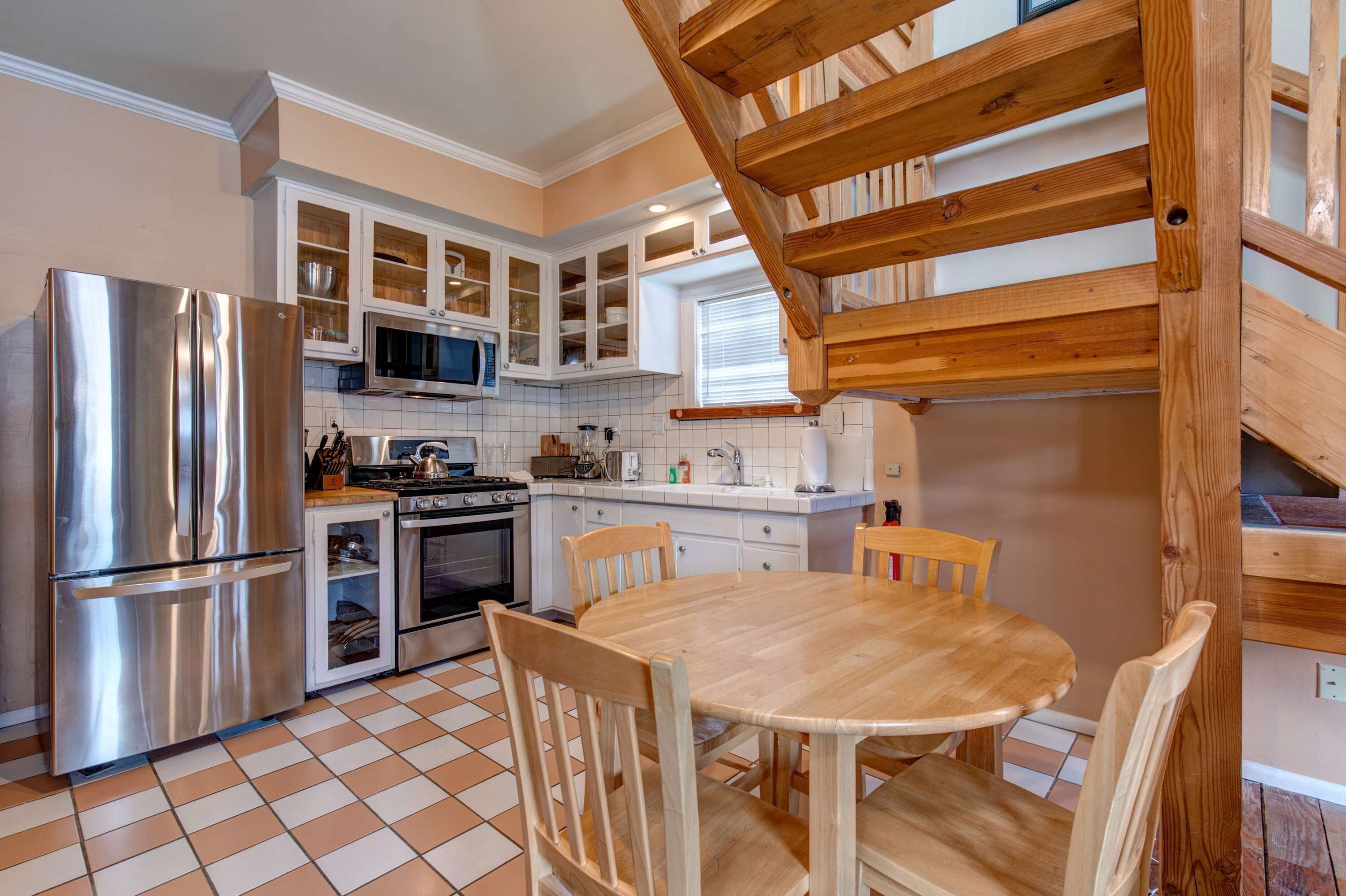 A kitchen with a stainless steel refrigerator, microwave, stove, and wooden dining table with chairs.